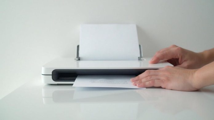 Main insère un document dans une imprimante blanche et compacte
